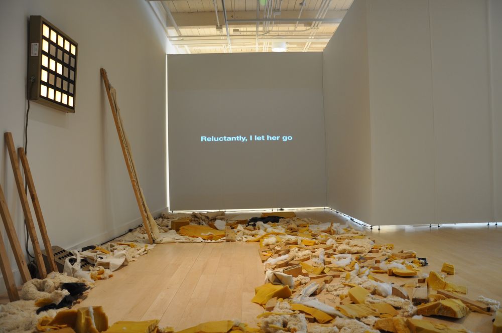 Couch to Geisha installation: debris from the dismantled couch on the floor, a light box and a projected line of text