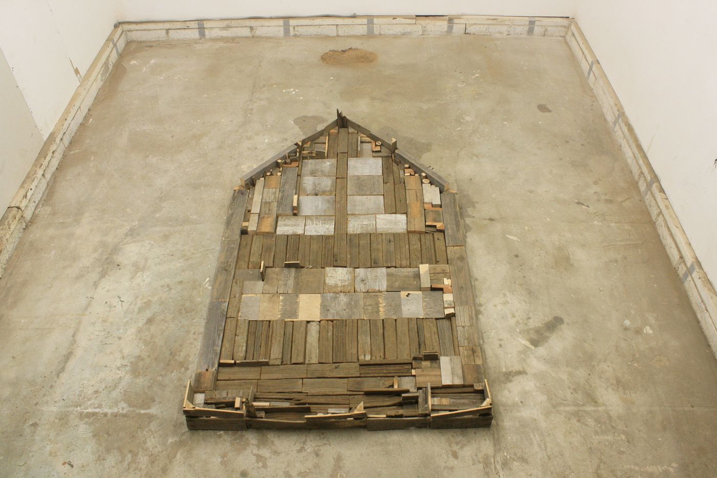 PileoToPenta: salvaged wood pieces laid on a concrete floor in the shape of a house